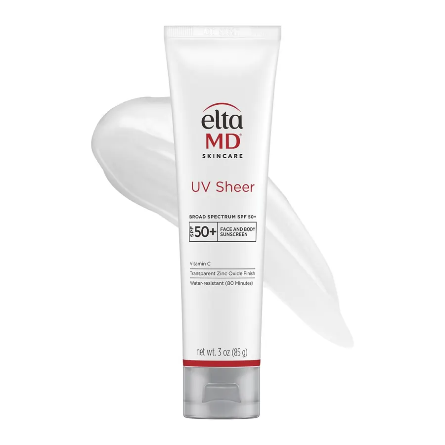 EltaMD UV Sheer bottle held in a woman's hand next to a bathroom sink with serums and moisturizer